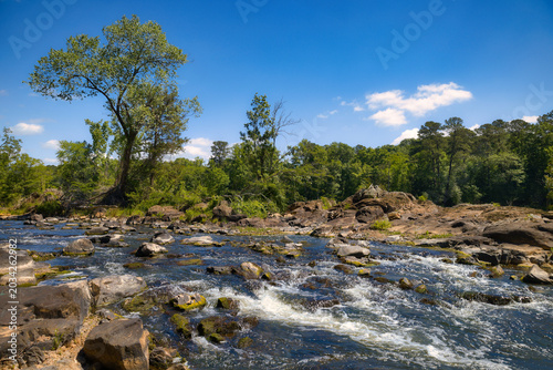 Schilderij op canvas A beautiful landscape under a blue sky of an American river in the mountains of Pittsboro, North Carolina with lots of rocks and bubbly whitewater rapids