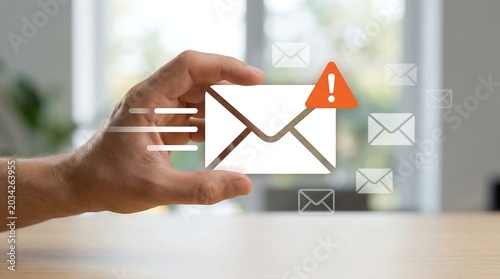 Hand holding physical paper envelope with orange hazard exclamation warning symbol representing potential email security threats and cybersecurity awareness in digital communication