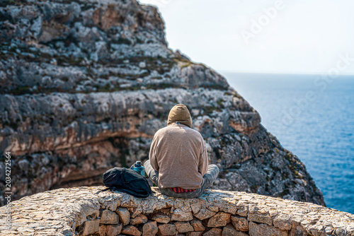 Photos Landscape shot from behind solo travelling man sat on ledge looking out over cli