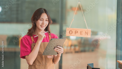 Cheerful Asian SME business owner preparing delivery packages for customers with shop open background.
