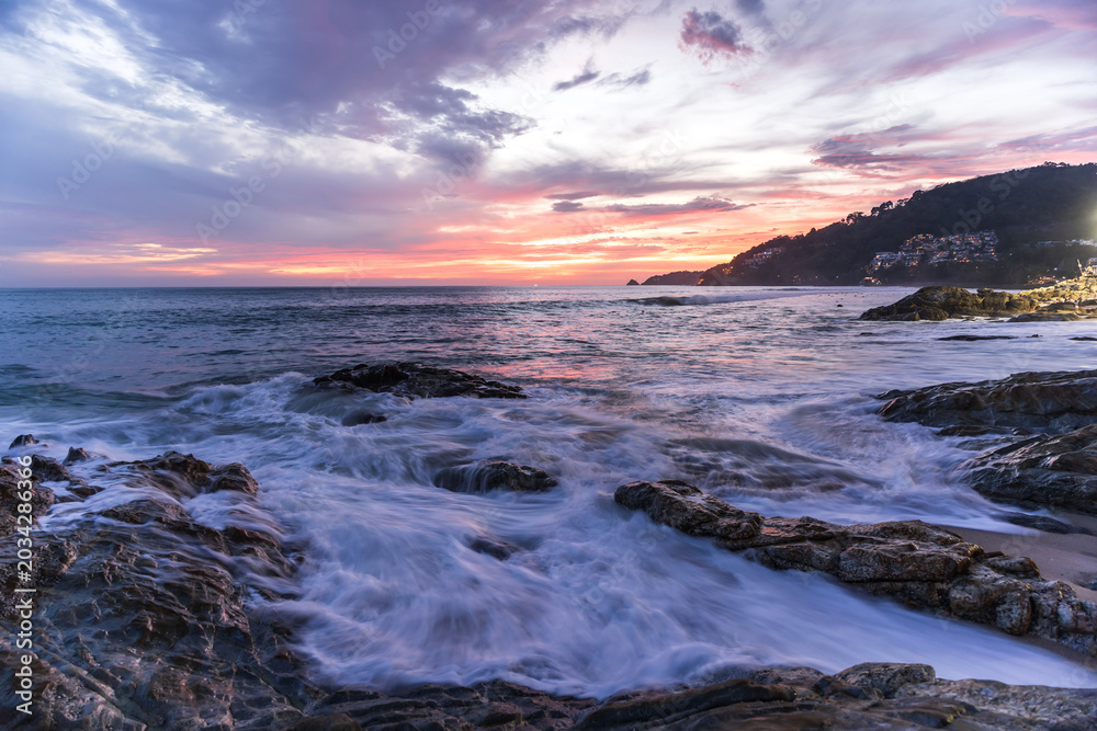 Fototapeta premium Rocky shoreline during vibrant twilight sunset over the ocean waves