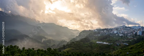 Panel kuchenny z motywem Beautiful panorama landscape of mountain valley with misty fog and hillside village under dramatic golden sky with sunrays at Sapa, Vietnam