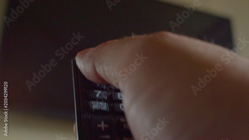 First-person view of a hand using a remote control to turn on a modern smart TV hanging on a wall, close-up, shallow depth of field.