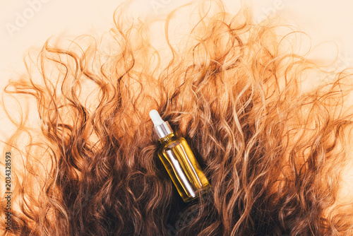 Shiny serum bottle surrounded by voluminous, wavy brown hair