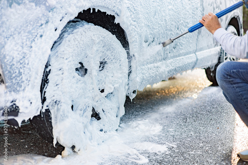 Tableau sur toile A person sprays foam onto a car wheel and side during a detailed cleaning proces