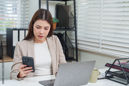 Asian female office worker checking smartphone and laptop for communication during work representing digital connection corporate productivity and professional lifestyle modern business concept