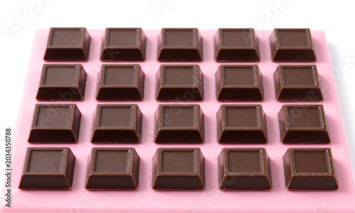 neatly arranged dark chocolate bar squares sit vibrant pink glossy surface subtly lit soft diffused studio lighting centered flat