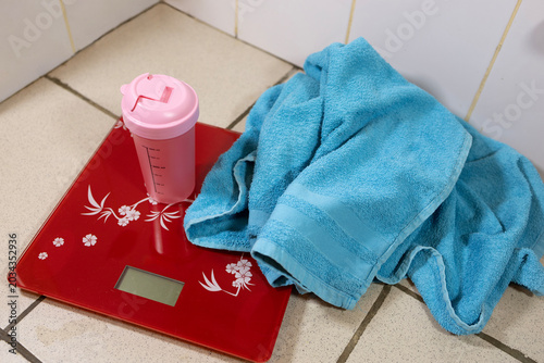 Fotografia Pink shaker bottle and blue towel on a red digital scale in a bathroom