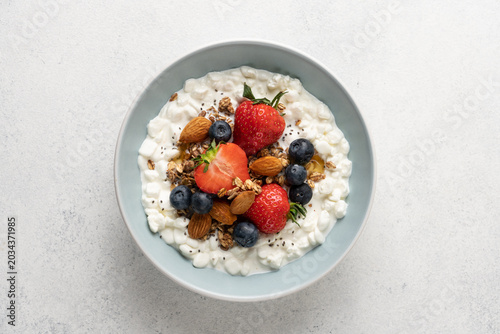 Fresh high protein cottage cheese berry bowl with blueberries, strawberries, chia seeds, granola and almonds served on light background with copy space