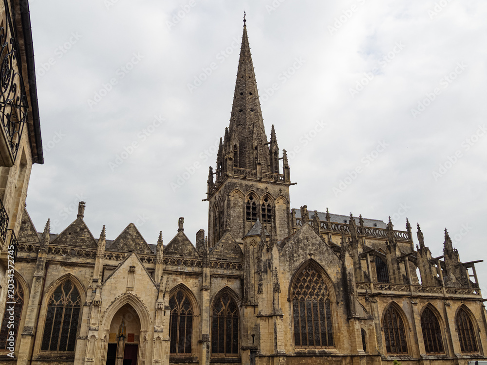 Fototapeta premium Iglesia Notre-Dame de Carentan, impresionante arquitectura romática y gótica en la Normandía francesa, con un campanario en punta y arcos en la fachada, viajando en verano de 2022