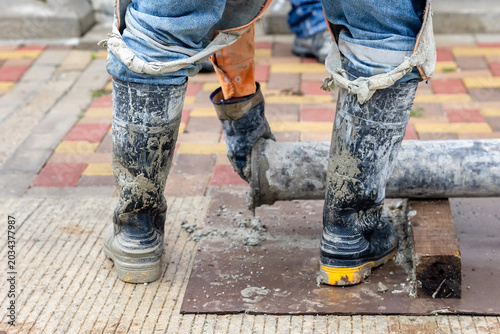 Картината върху платно Construction worker in muddy rubber boots disconnecting concrete pump pipeline d