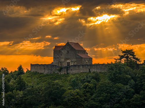 Cisnădioara fortress in Sibiu, Transylvania. aerial view of the historic stone fortified church of Cisnadioara on a green hill, surrounded by defensive walls under a dramatic sunset sky with sun rays
