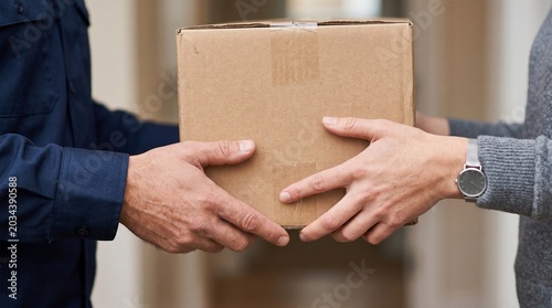 Close-up view of a delivery person's hands carefully passing a brown cardboard package to a customer, illustrating the secure and efficient process of parcel delivery and receipt in modern logistics