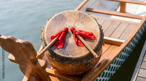 Traditional Chinese dragon boat drum with red mallets resting on the wooden bow near water