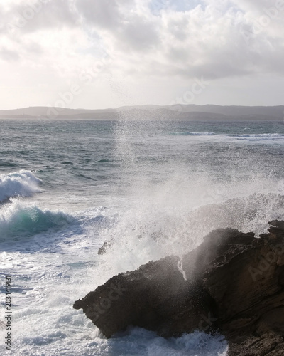 Waves crash against rocks by the ocean under a cloudy sky during the day