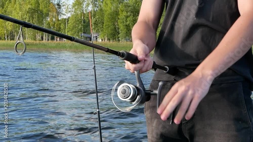 Young male fisherman catching fish with a spinning rod on a calm lake during a sunny summer day.