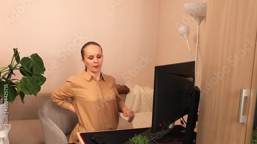 A focused young white woman is working on a computer at her desk. Her back hurts. She was tired of work.