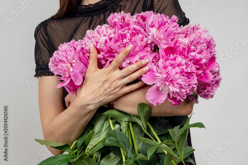 Fotografie Close-up of female hands hugging a large armful bouquet of fresh pink peonies against a grey background