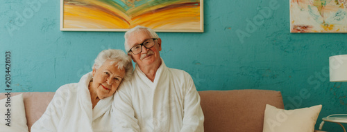 фотографія Portrait of happy senior couple sitting together in bathrobe on sofa