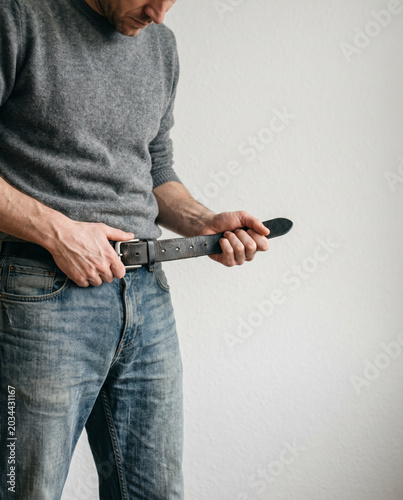 Konzeptbild zur Redewendung „den Gürtel enger schnallen“, bei dem eine Person wortwörtlich ihren Gürtel enger zieht.