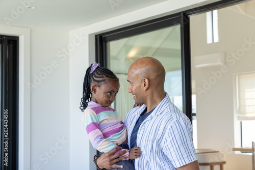 Photos Father holding child daughter, smiling and looking down in bright living room ne