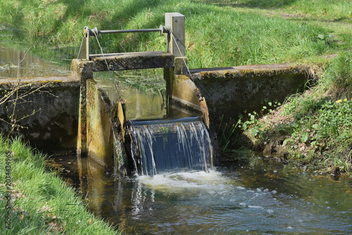 Fotografi Small historic concrete and metal weir water control gate structure on a stream