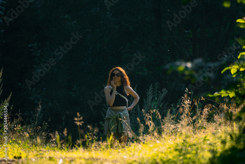 Fotografia Young woman wearing sunglasses hikes through a tranquil forest at sunset, savori