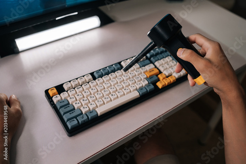 Close-up of repairman cleaning computer mechanical keyboard on white desk, using electric air duster to remove dust and debris from keys as part of regular maintenance and tech hygiene, close-up.