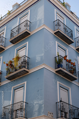 Corner view of a vibrant blue apartment building with a street sign for Calle San Luis in Seville
