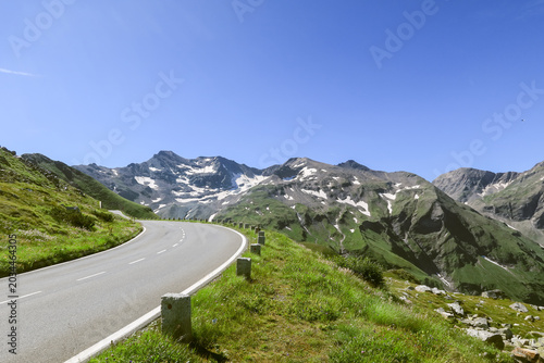 Foto Empty curving mountain road with snow patched peaks