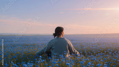 Donna seduta in meditazione in un campo di fiori blu al tramonto