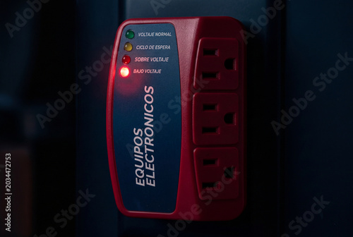 Primer plano macro de un protector de voltaje electrónico enchufado, con la luz LED roja de alerta encendida en la opción de 
