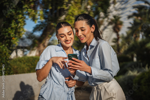 Obraz na płótnie Two smiling women sharing content on smart phone