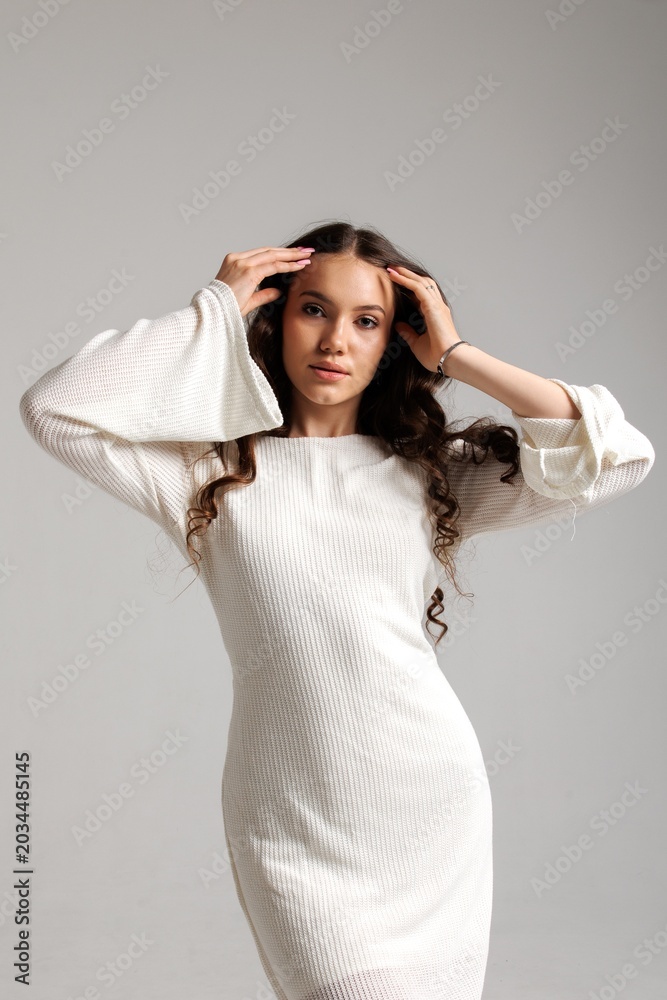 Fototapeta premium Model poses in a white dress with bell sleeves against a neutral background in a studio setting