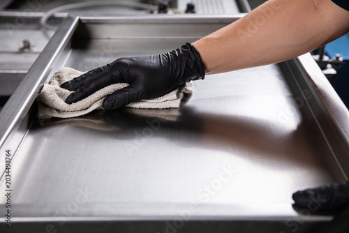 Картината върху платно Hand in black glove wiping down a shiny stainless steel surface with a cloth