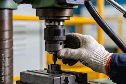 Fotografie Worker's gloved hand operating a drill press for precision metalworking
