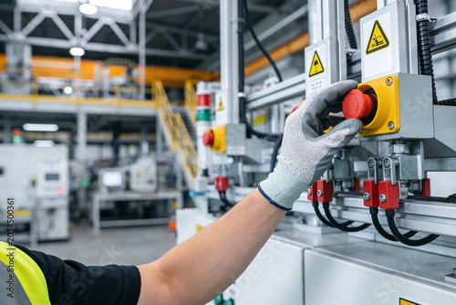 Foto Worker in safety gloves operates industrial machinery with emergency stop button