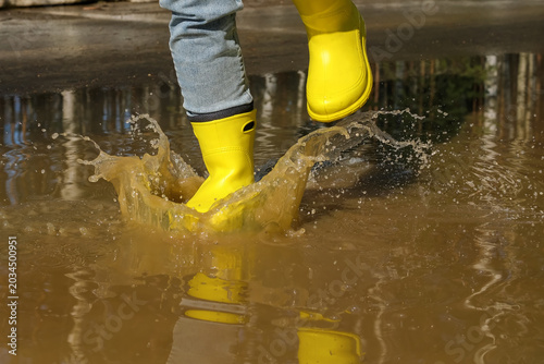 Foto Woman splashing muddy spring puddle while walking in bright yellow waterproof bo