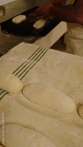 Male baker's hands taking proofed bread dough from a floured cloth and placing it on a baking sheet, preparing it for the oven