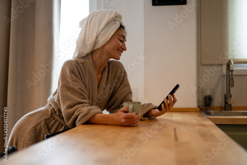 Foto Smiling woman in bathrobe with towel on head talking on smartphone while holding