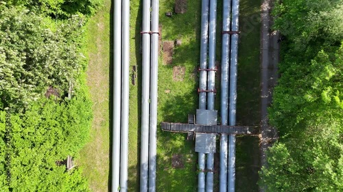 Aerial view of industrial pipes for gas, water, and oil running parallel across a green landscape, showcasing a continuous flow of infrastructure and nature in harmony