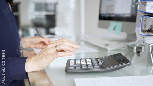 Картината върху платно Woman calculating finances on a desk in a modern office, working on accounting, banking, and budget planning