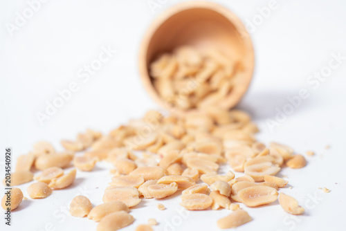 Peanuts in a wooden cup rest on a white background, creating a warm and rustic food-themed scene.
