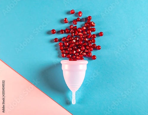 White Menstrual Cup Overflowing with Red Beads on Blue and Pink Background