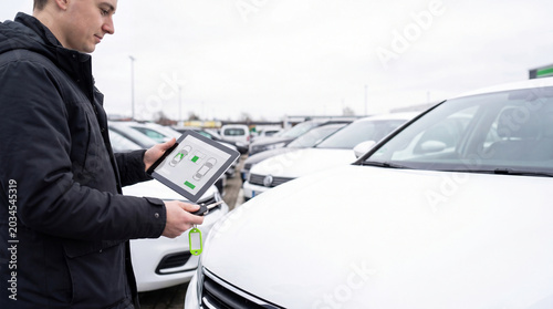 Man using tablet to check vehicle status at rental agency. Manager inspecting car for rent with digital application. Automobile fleet management and smart transport service concept.