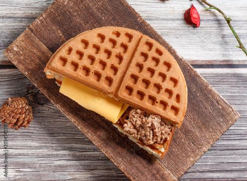 Obraz na płótnie A delicious waffle sandwich with cheese and tuna on a wooden board with pinecone