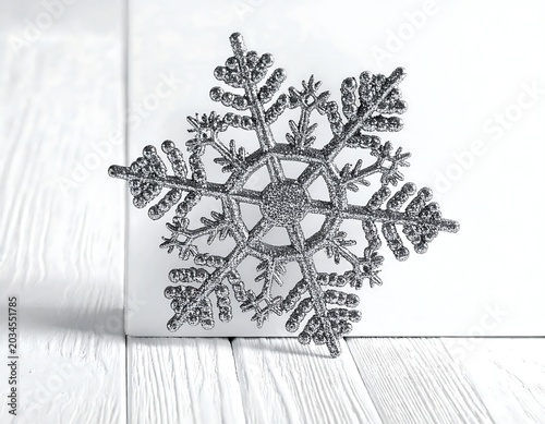 Glittering Silver Snowflake Ornament Resting on White Wooden Surface