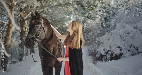 Young woman stroking her horse in a snowy forest
