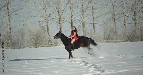Woman in red dress horseback riding in winter wonderland