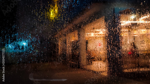 Schilderij op canvas Rain drops on window glass at night with blurred city lights background